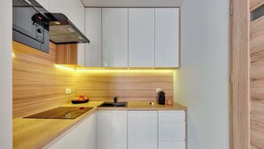 Une cuisine moderne avec des meubles blancs, un plan de travail en bois, un four encastré et une machine à café.