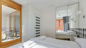 Hotellihuone, jossa on sänky, kylpyhuone peilillä ja pesualtaalla, liukuovet, jotka johtavat parvekkeelle, sekä pöytä ja tuolit ulkona.