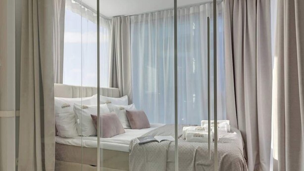 Un dormitorio moderno con una cama grande, cortinas translúcidas y vistas al cielo.