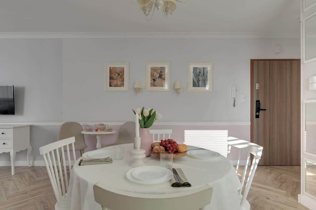 A dining area with a round table, white chairs, a television, and framed pictures on the wall.