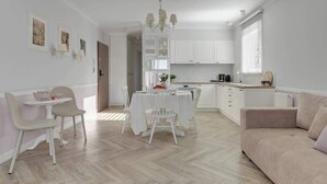 Una cocina moderna con armarios blancos, un comedor con mesa y sillas blancas, y una sala de estar con sofá.