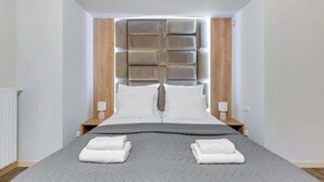 Ein modernes Hotelzimmer mit einem großen Bett, einem Kopfteil mit integrierter Beleuchtung, Nachttischen mit Lampen und ordentlich gefalteten Handtüchern auf dem Bett.