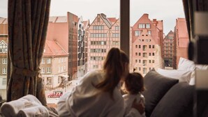 Et værelse med udsigt til bygningerne, en seng med puder og et vindue med gardiner.