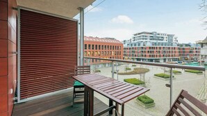 Un balcón con mesa y sillas, vista a edificios modernos y cielo despejado.
