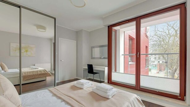 Un dormitorio con cama, escritorio, silla y un ventanal con vistas a edificios.