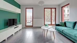 Una sala de estar moderna con televisor, un sofá, una mesa de centro y ventanas amplias.