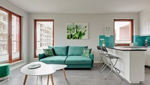 Una sala de estar moderna con un sofá verde, una mesa de centro blanca y una cocina con salpicadero azul turquesa.