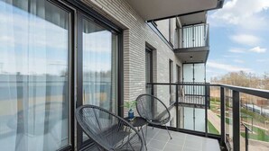Ein Balkon mit zwei Stühlen, einem Blumentopf und Blick auf ein Gebäude mit großen Fenstern.