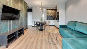 Un soggiorno moderno con una televisione a schermo piatto, un divano verde acqua, una zona pranzo con un tavolo rotondo e una cucina sullo sfondo.