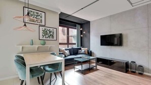 A modern living room with a sofa, a TV, a dining table with chairs, and a coffee table. - Nº 75 | Pool, SPA & Gym (Gdańsk)