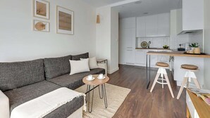 A modern living room with a grey sofa, a small round table with cups, a kitchen area with white cabinets, and a bar stool. - Nadmotławie 45 | Riverside | Sauna & Gym (Gdańsk)