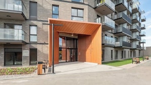 A modern building with a wooden entrance canopy, multiple balconies, and a paved walkway. - Nadmotławie 45 | Riverside | Sauna & Gym (Gdańsk)