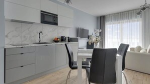 Una cocina moderna con microondas integrado, un lavamanos y un comedor con mesa blanca y sillas negras.