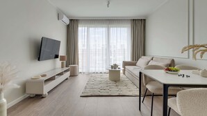 Uma sala de estar moderna com televisão de tela plana, sofá, mesa de jantar e uma grande janela com cortinas.
