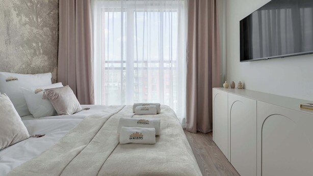 Quarto de hotel com cama, televisão, guarda-roupa e janela com cortinas.
