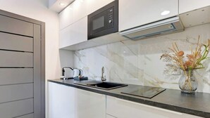 A modern kitchen with a built-in microwave, a sink, and a vase with dried flowers on the countertop. - Granaria B23 | Perfect Location | Old Town (Gdańsk)