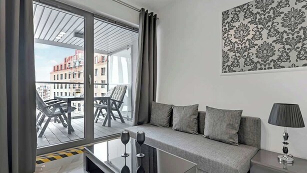 A modern living room with a sofa, a glass coffee table, and a view of the city through large windows. - Granaria B23 | Perfect Location | Old Town (Gdańsk)