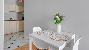 Eine moderne Küche mit weißen Schränken, einem weißen Esstisch mit zwei gewobenen Unterlagen und einer Vase mit weißen Blumen.