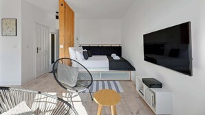 Quarto moderno com cama, televisão, cadeira e uma pequena mesa.