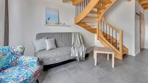 A modern living room with a grey sofa, a colorful armchair, a wooden staircase, and a painting on the wall. - Stodoła 1 | Nad Morzem | Jastrzębia Góra (Jastrzębia Góra)