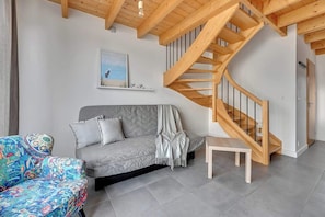 Ein modernes Wohnzimmer mit einem grauen Sofa, einem farbenfrohen Sessel, einer Holztreppe und einem Bild an der Wand.