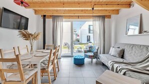 A modern interior with a wooden ceiling, a dining area with a table and chairs, a sofa, and a TV mounted on the wall. - Stodoła 1 | Nad Morzem | Jastrzębia Góra (Jastrzębia Góra)