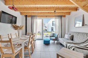 Ein modernes Interieur mit Holzboden, einem Essbereich mit Tisch und Stühlen, einer Couch und einem an der Wand befestigten Fernseher.