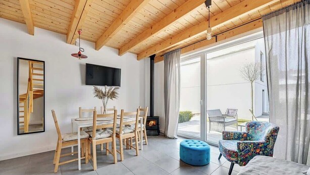 A modern living room with a wooden ceiling, a dining area with wooden chairs, a blue ottoman, a sofa, and a TV mounted on the wall. - Stodoła 1 | Nad Morzem | Jastrzębia Góra (Jastrzębia Góra)