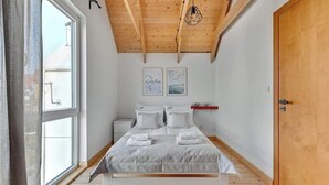 A bedroom with a wooden ceiling, a bed with white bedding, two framed pictures on the wall, and a window with curtains. - Stodoła 1 | Nad Morzem | Jastrzębia Góra (Jastrzębia Góra)