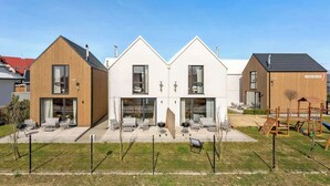 Ein modernes, zweistöckiges Haus mit Terrasse, Sitzgelegenheiten im Freien und einer Spielanlage.