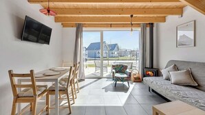Ein modernes Wohnzimmer mit einer Couch, einem Esstisch mit Stühlen, einem an der Wand befestigten Fernseher und einem Kamin.