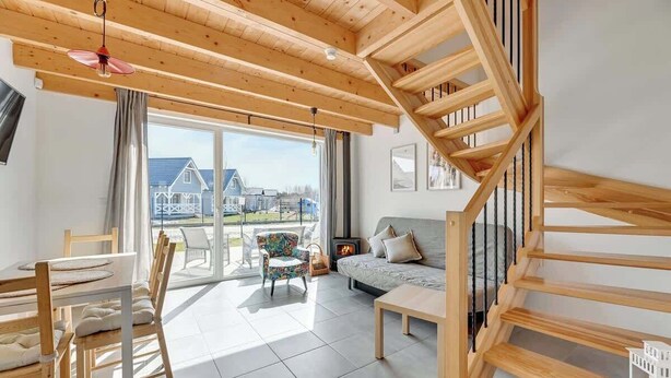 Ein geräumiger Wohnbereich mit einer Holztreppe, einem Esstisch mit Stühlen, einem Sofa und Blick ins Freie.