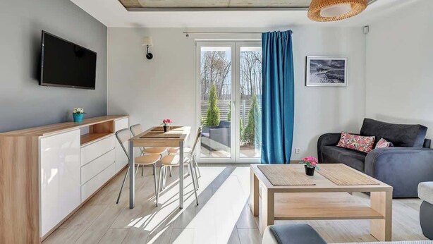 Una sala de estar moderna con un televisor de pantalla plana, un comedor con sillas, un sofá y un amplio ventanal con cortinas.