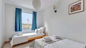 Una habitación con dos camas, una ventana con cortinas, una lámpara de pared y un cuadro enmarcado.