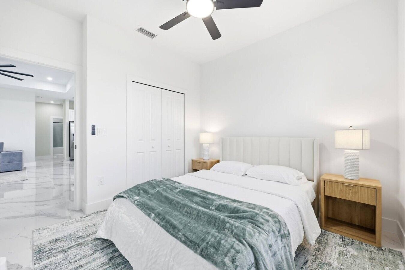 A modern bedroom with a bed, bedside lamps, a ceiling fan, and a door.