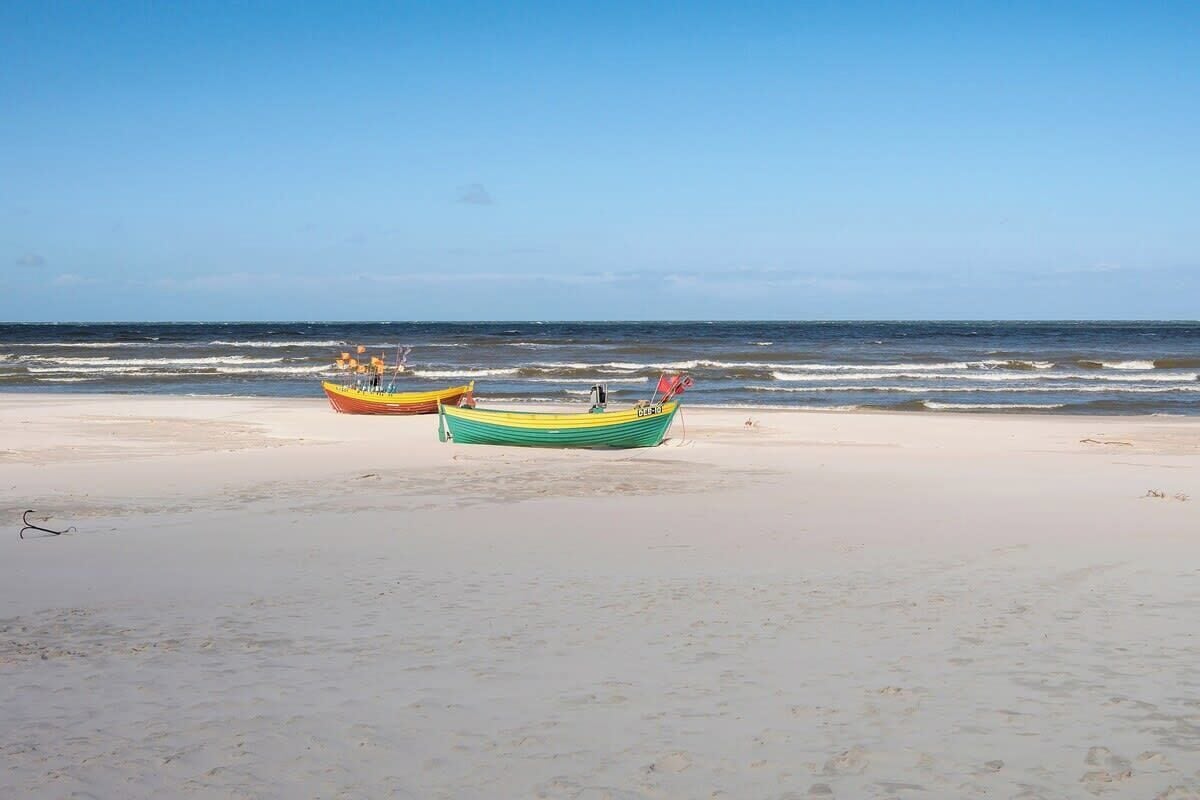 Una playa con dos barcos en la arena, cielo despejado y el océano al fondo.