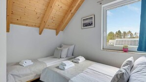 A bedroom with two beds, a window with a view, and a ceiling with wooden beams. - Dębki 6 | Rodzinny Apartament | Nad Morzem (Dębki)