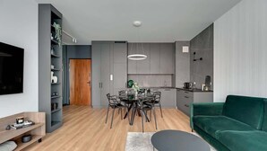 Een moderne keuken met grijze kastjes, een eethoek met een ronde tafel en een groene bank.