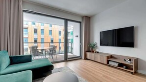 Een moderne woonkamer met een bank, salontafel, televisie en een schuifdeur die leidt naar een buitenbalkon.
