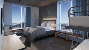 Ein modernes Hotelzimmer mit Bett, Schreibtisch und Etagenbett, großen Fenstern mit Blick und einem Kopfteil mit integrierter Beleuchtung.