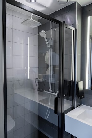 Ein modernes Badezimmer mit einer ein Glaswand abgetrennten Dusche, einem weißen Waschbecken und einem großen Spiegel.