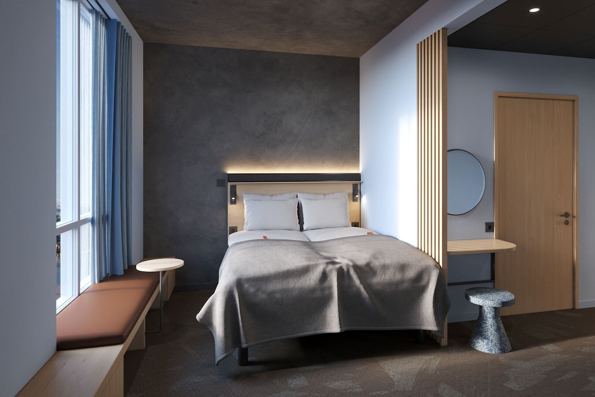 Ein modernes Schlafzimmer mit einem Bett, Nachttischen, einer Bank, einem runden Spiegel und einer Holztür.