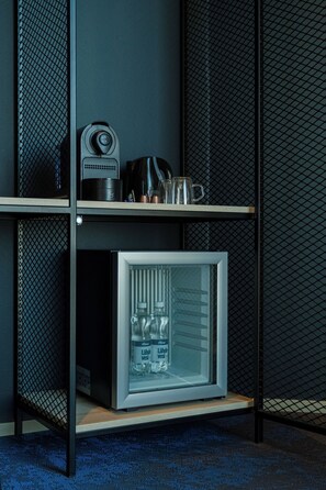 Un refrigerador compacto con puerta de vidrio, un estante pequeño encima y un panel de malla metálica.