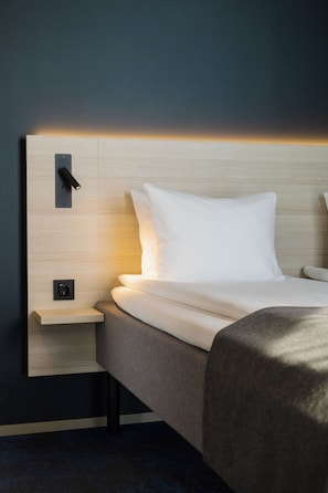Et hotelværelse med en seng, et natbord og en lampe fastgjort på væggen.