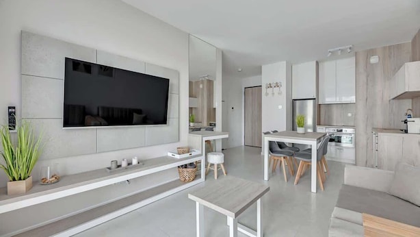 Ein modernes Wohnzimmer mit Flachbildfernseher, ein Essbereich mit Tisch und Stühlen sowie eine Küche mit Schränken und Geräten.