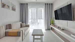 Ein modernes Wohnzimmer mit Sofa, Couchtisch, Fernseher und einem Balkon mit Vorhängen.