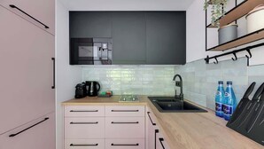 A modern kitchen with a black microwave, a coffee maker, and a sink. There are two bottles of water on the counter. - Dwie Motławy 30 | River View | City Center (Gdańsk)