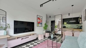 A modern living room with a large flat-screen TV, a pink rug, and a checkered floor. - Dwie Motławy 30 | River View | City Center (Gdańsk)