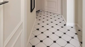 Ein Flur mit einer weißen Tür, einem gerahmten Bild an der Wand, einer grünen Pendelleuchte und einem gefliesten Boden.
