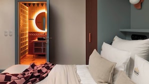 Een slaapkamer met een bed, kussens, een nachtkastje en een bedtafel.